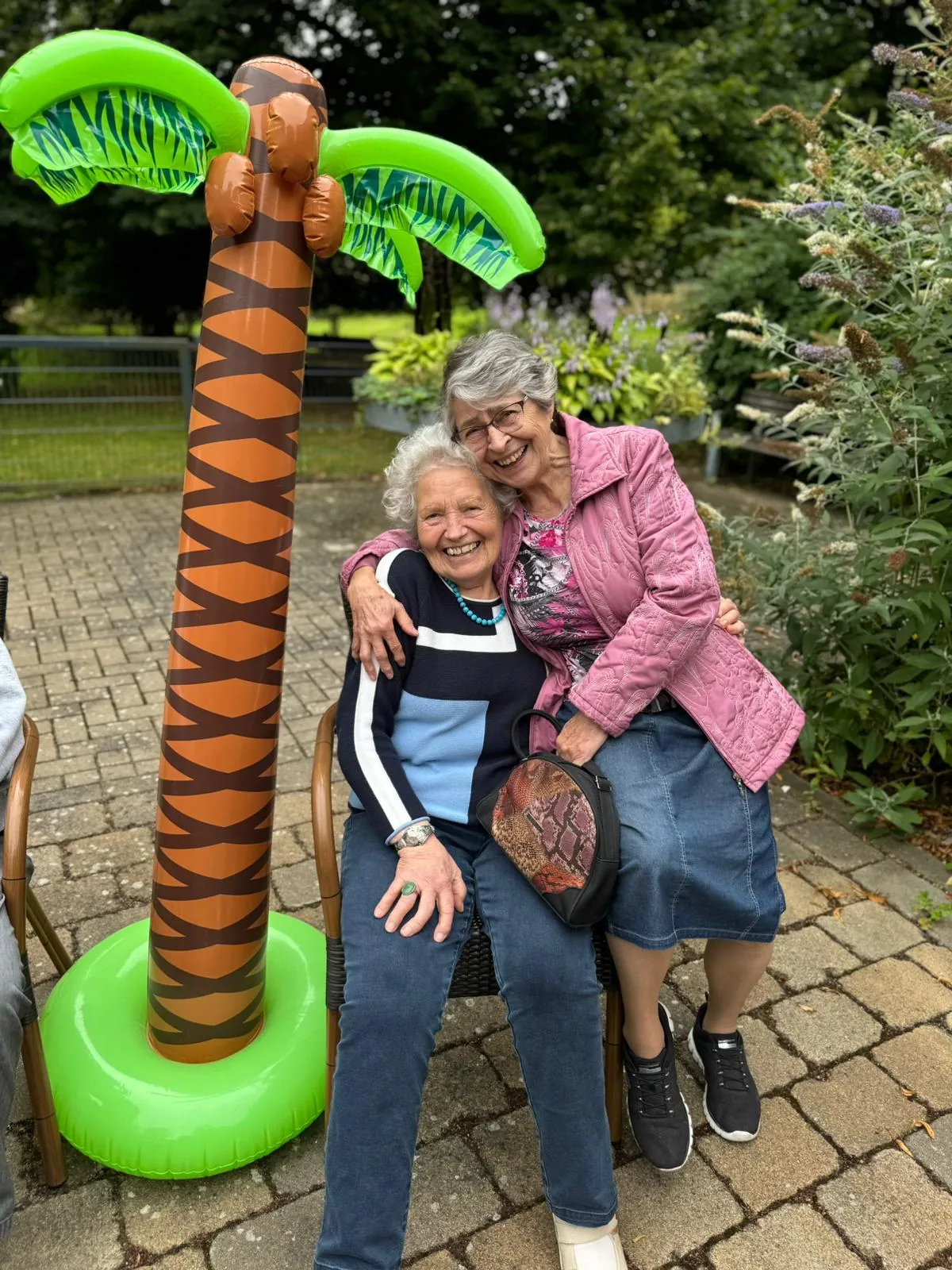 Zwei Seniorinnen umarmen sich lachend im Garten des TagesNests